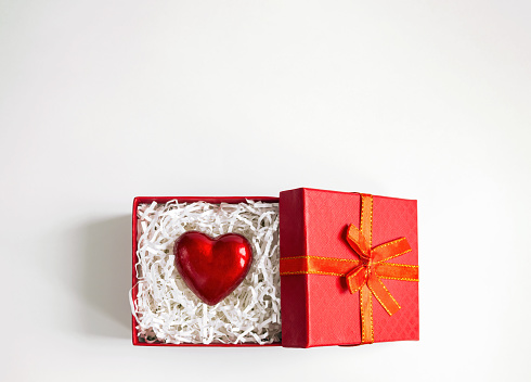 Red heart between crinkle cut paper in gift box on white background. Valentine day card with copy space, top view
