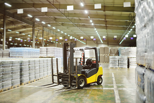 Yellow loader on the background of a huge industrial food warehouse with plastic PET bottles with beer, water, drinks.