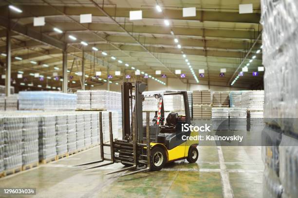 Loader On The Background Of A Huge Industrial Food Warehouse With Plastic Pet Bottles With Beer Water Drinks Stock Photo - Download Image Now