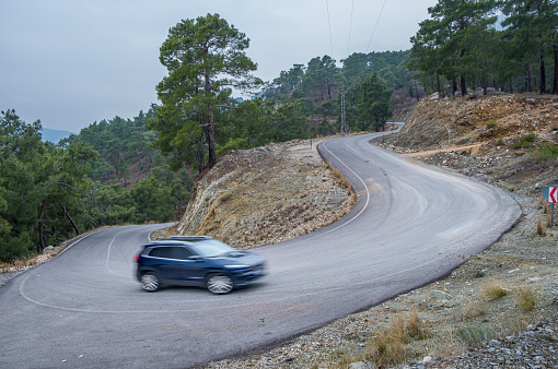 Hard winding asphalt road. Forest around the road. Closed air. Mountains in the distance.Slow shutter shooting