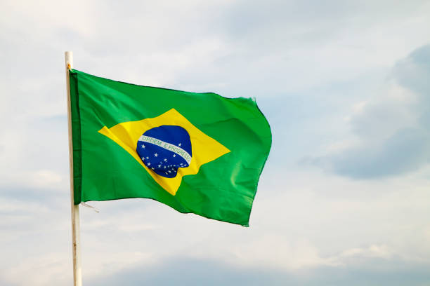 istock Brazilian flag on a blue sky with clouds background 1296039812