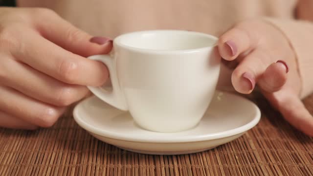 Hand of a woman drinking coffee with a white ceramic cup in a cafe.