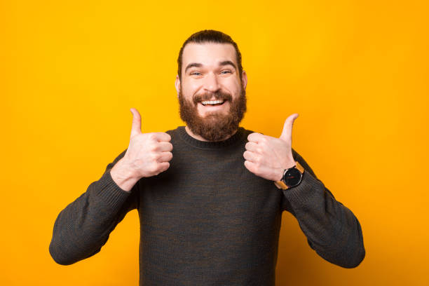 istock Cheerful handsome bearded man standing over yellow background and showing thumb up 1296041937