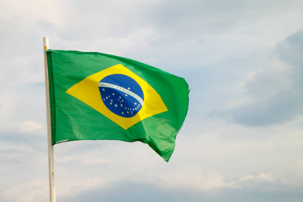 istock Brazilian flag on a blue sky with clouds background 1296042003