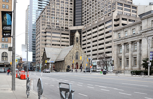 Toronto, Canada - November 19, 2020: The Queens Park route south of Bloor Street West is almost empty on a weekday morning during COVID-19. Background shows the historic Church of the Redeemer with a backdrop of commercial and hotel towers along Bloor Street West and Avenue Road.