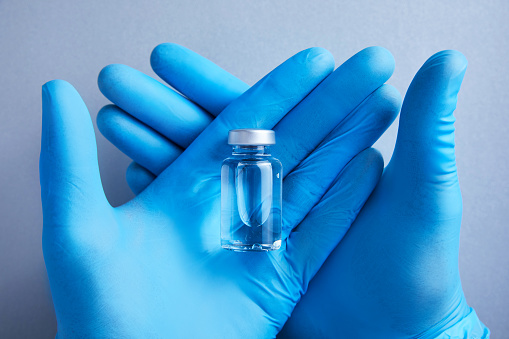 Gloved hands carefully hold a glass vial of vaccine for science