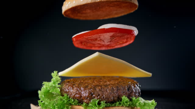 Making a Hamburger with Falling Barbecued Beef Patty, Cheddar Cheese, Sesame Bun and Vegetables in Slow Motion