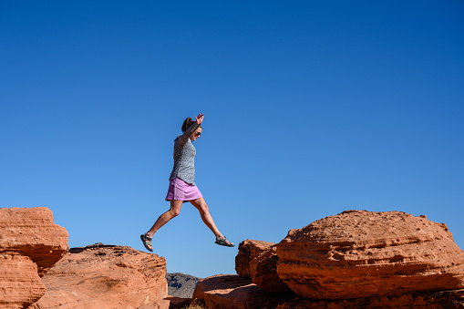 Woman Jumps Over Sandstone Boulders against blue sky