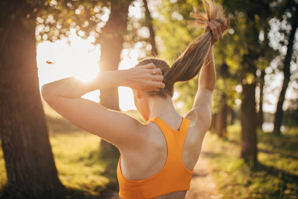 Fit woman tying ponytail on her hair in nature One woman, fit young female standing alone in nature, tying ponytail on her hair on a sunny day. woman tying hair in ponytail getting ready for exercising stock pictures, royalty-free photos & images