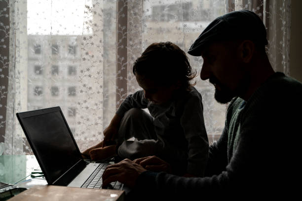 il padre, che lavora da casa, è accompagnato dal figlio alla sua scrivania. - laptop adult curtain business foto e immagini stock