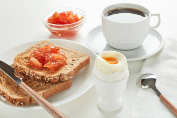 istock Boiled egg, toasts with apple jam and cup of coffee on white background, Selective focus on boiled egg 1296066317
