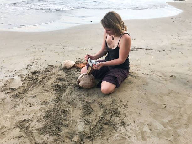 istock Woman tries to open a coconut on a sandy beach 1296068711