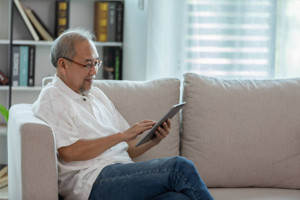 istock Happiness elderly asian man sitting on sofa and using computer tablet and smile at home,Senior lifestyle at home concept 1296071856