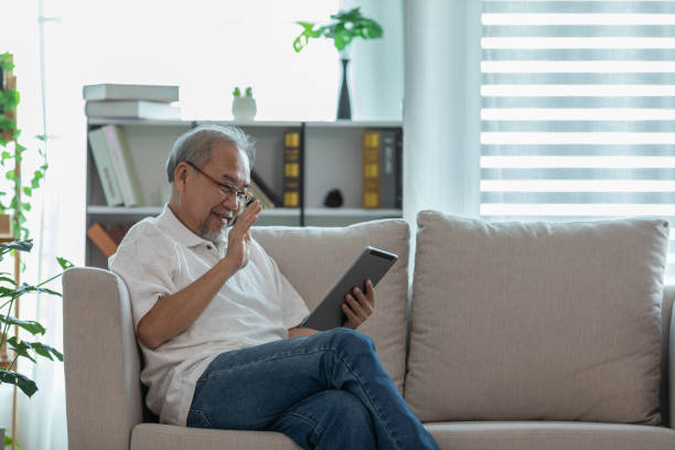istock Happiness elderly asian man sitting on sofa and using computer tablet VDO Conference online meeting with family and smile at home,Senior lifestyle at home concept 1296071861