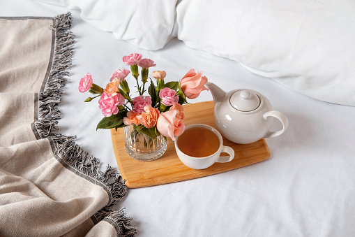 Tray of tea on bed. White bedding sheets with blanket and pillow. Breakfast in bed. Warm and cosy scandinavian hygge concept - cup of tea.