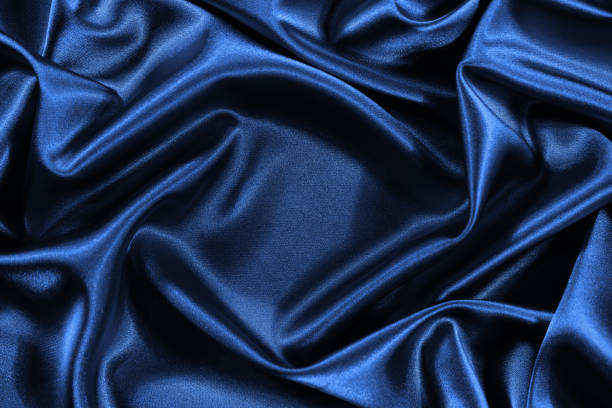 istock Blue silk satin background. Shiny fabric with wavy folds. 1296084987