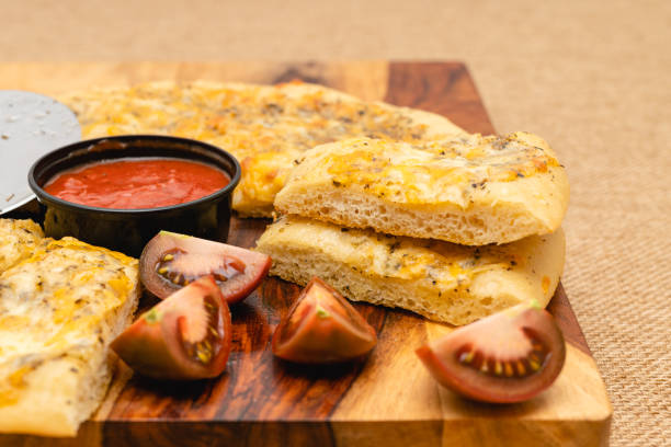 istock Classic cheesy bread topped with herb garlic spread, and cheese blend served with marinara sauce and fresh sliced tomatoes close up on rustic background 1296087612