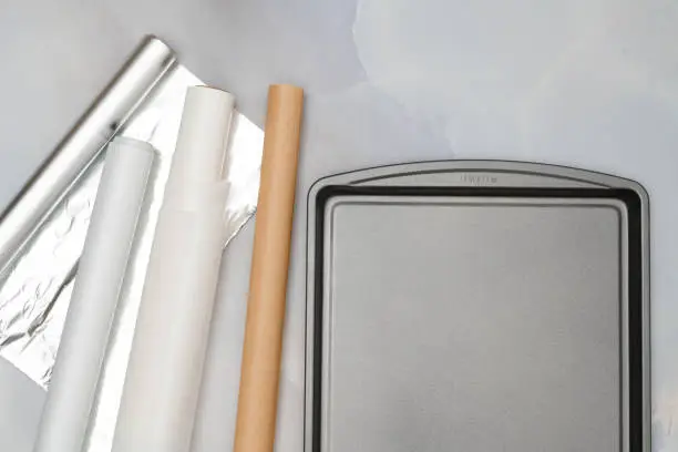 Photo of Different type of paper for baking needs and baking pan on marble background. Parchment paper, foil, wax paper, baking sheet close up