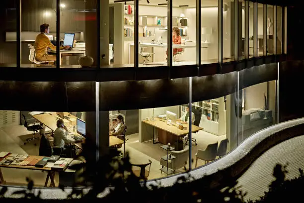 Bi-level exterior view of five design professionals working independently at computer monitors in modern office at night.