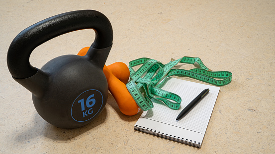 Fitness background. A set of accessories for training at home during quarantine - 16 kg kettlebell, a pair of dumbbells, a notepad with a pen and a measuring tape to track progress