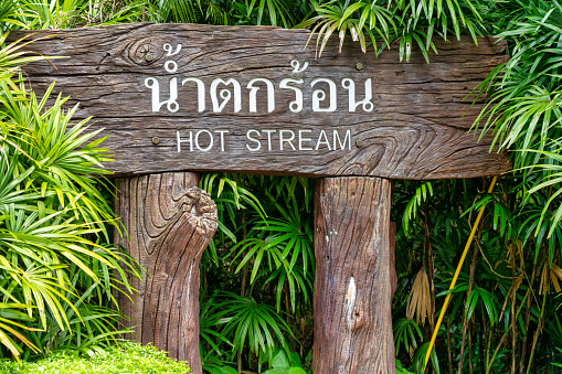 Klong Thom, Krabi province, Thailand - September 16, 2020:  A wooden entrance sign saying ‘Hot Stream’ sits in the jungle pointing the way to a popular natural hot springs.