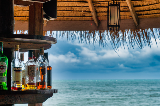 Ko Lanta, Krabi province, Thailand - September 24, 2020:  A tropical beach bar with alcohol spirit bottles and the blue sea in the background.