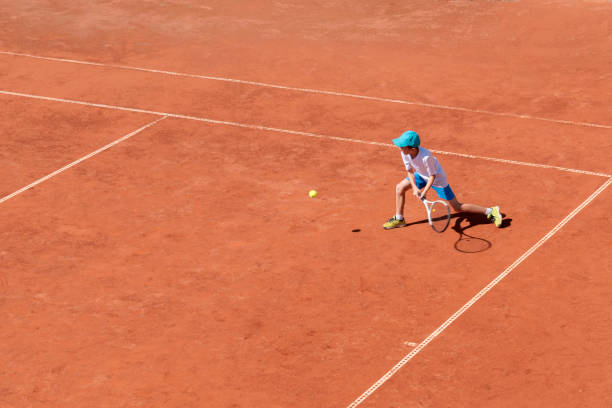 un garçon joue au tennis sur un court de tennis extérieur. l’enfant est concentré et concentré sur le jeu. match. sport actif. - tennis child teenager childhood photos et images de collection