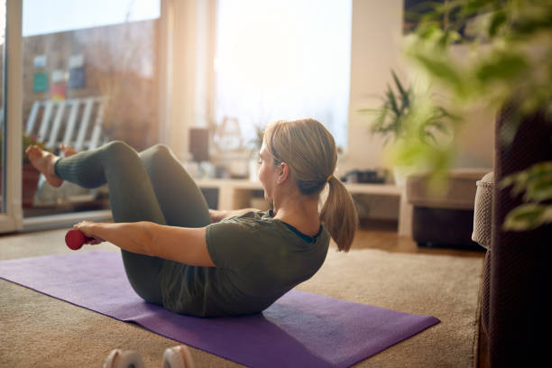 istock Athletic woman using hand weights while doing sit-ups in the living room. 1296103233