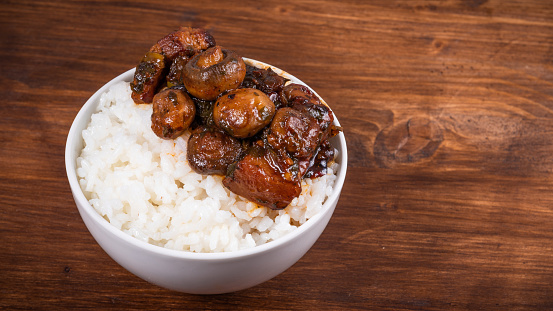 Small bowl with spicy stewed pork with mushrooms in oriental style with spices, hot peppers and boiled rice on a wooden table - top view, copy space, close-up