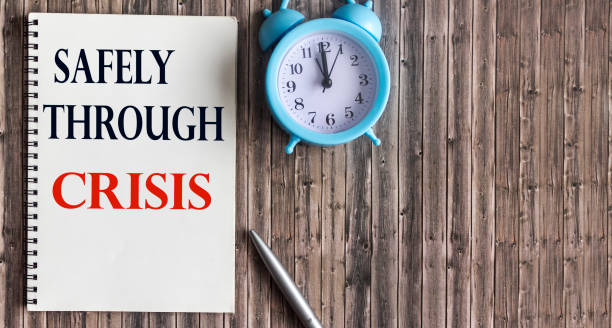 istock Pen, alarm clock and notebook with the text SAFELY THROUGH CRISIS 1296106267