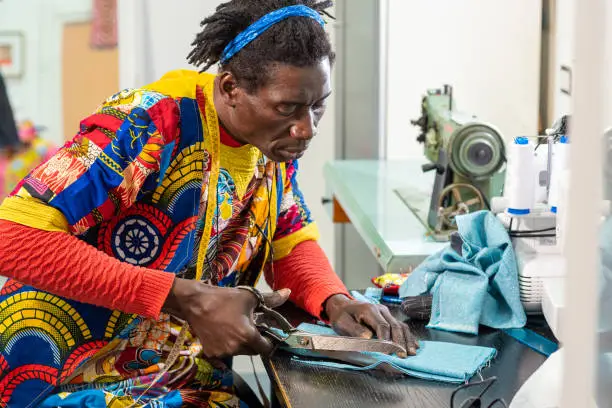 Photo of african tailor from senegal at work in his workshop, handcrafted production of european fashion clothes with african wax fabrics, concept of diversity and integration, new small socialbusiness