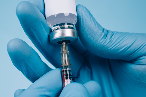Médico o científico que mantiene la dosis del vial de vacuna común con jeringa contra fondo azul con espacio de copia - concepto de vacunación global. Imagen de maqueta. Enfoque selectivo photo