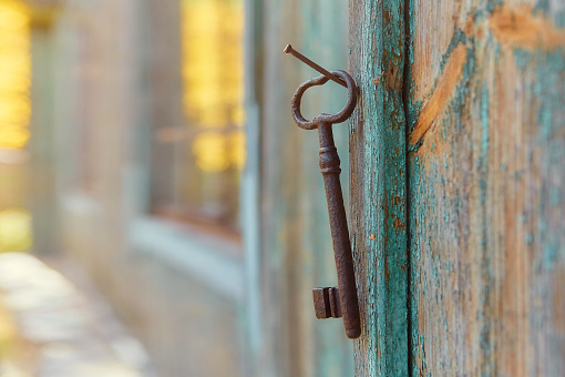 An old iron retro key hanging on a nail against the wall of a rustic wooden house, the concept of a secret, inheritance, opportunity