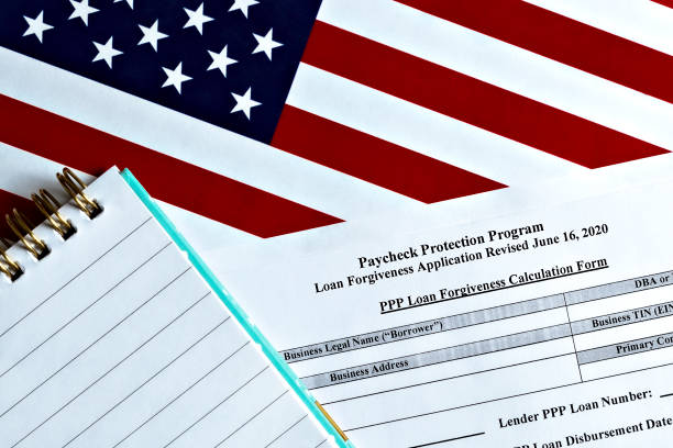 istock close-up of paycheck protection program loan forgiveness application form revised topview, on a background of United States flag. paycheck protection program new round. 1296110264