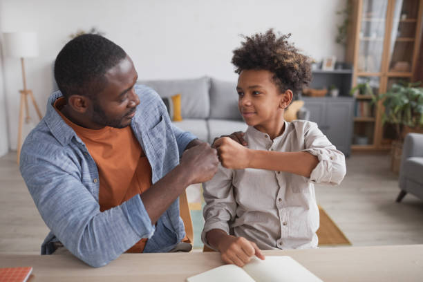 Father and Son Fistbumping Portrait of African-American father fist bumping smiling son while doing homework together at home preadolescents stock pictures, royalty-free photos & images