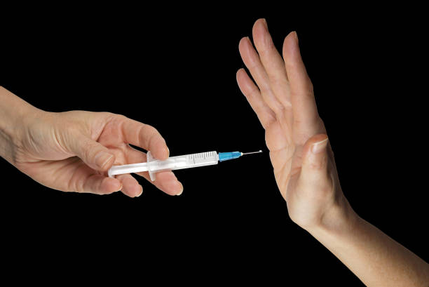 Thanks but I don't want your vaccine hand holding a vaccine syringe opposite a hand in NO position against black background with copy space herd immunity photos stock pictures, royalty-free photos & images
