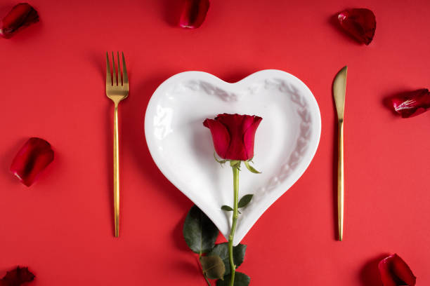 istock Romantic table setting for Valentines day made with golden knife and fork, heart shaped plate and rose on red background 1296115822