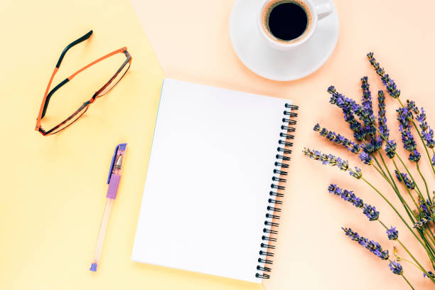 istock Blank notepad on yellow background with lavender flowers, coffee cup, pen and glasses. Top view, flat lay 1296116074