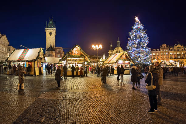 Christmas market at Old Town Square of Prague, Czech Republic Prague, Czech Republic - December 11, 2019: Panoramic view of Christmas market at Old Town Square with the city's main Christmas tree in dusk. The Gothic Old Town Hall and Baroque St. Nicholas Church are visible in the background. Unknown people walk around the market stalls. st nicholas church prague stock pictures, royalty-free photos & images