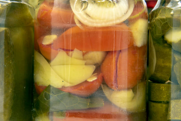 Full frame of a jar with pickles, cucumbers, peppers and tomatoes as a backdrop. Home-made preparations.