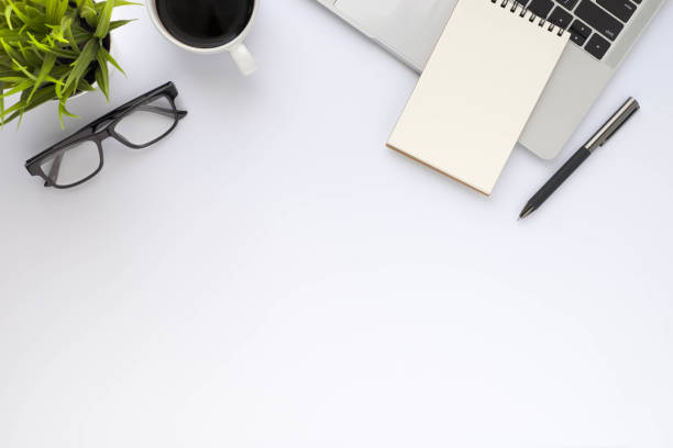istock Workplace in office with white desk. Top view above of keyboard computer with coffee cup and glasses. Space for modern creative work of designer. Flat lay with copy space. Business-finance concept. 1296119744