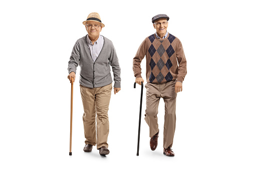 Full length portrait of two elderly men with canes walking towards camera isolated on white background