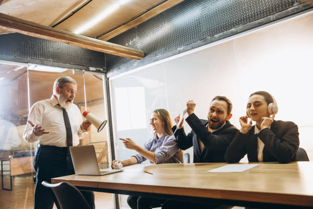 istock Angry boss with megaphone screaming at employees in office, scared and annoyed colleagues listening at the table 1296127414