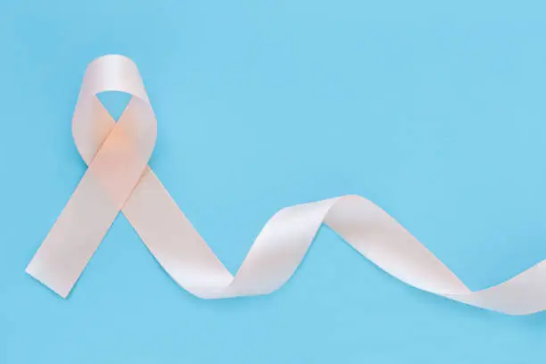 Peach color ribbon curl on pastel blue isolated background with copy space, symbol for Uterine and Endometrial cancer awareness, World Cancer Day. Healthcare or hospital and insurance concept.