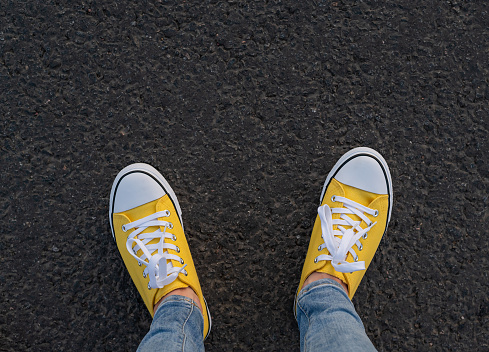 Top view of yellow sneaker shoes standing on asphalt walkway.