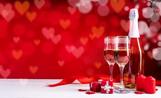 Valentines Day. Champagne flutes, candles and red hearts on beautiful bokeh background