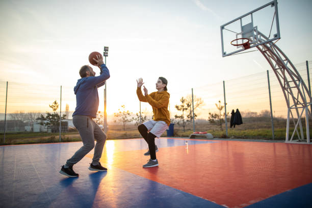 père et fils jouant au basket-ball sur le terrain extérieur - parent teenager caucasian teenage boys photos et images de collection