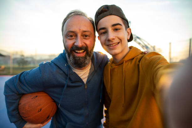 padre e figlio si fanno selfie sul campo da basket all'aperto - family adult portrait parent foto e immagini stock