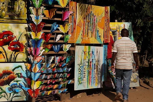 Kpalimé, Togo - November 23, 2019: Artist presenting a painted picture. He sells his beautiful colorful paintings in a small roadside studio and workshop in Kpalimé, Togo, West Africa.
