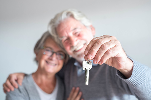 couple of two seniors after buy a new house or car and go to live together - man holding a key and mature man and woman looking at it